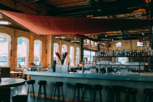 Man sieht einen lange Bar mit vielen Stühlen in einer alten Industriehalle.