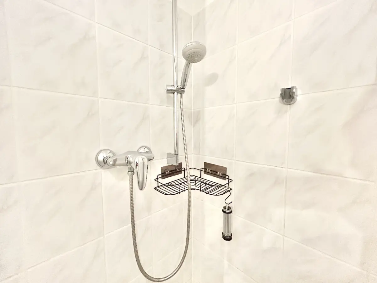 ferienwohnung-cottbus-green-apartment-bad-dusche Moderne Duscharmatur und praktische Eckablage im hell gefliesten Badezimmer des Green Apartments – Ihre gepflegte Ferienwohnung in Cottbus.