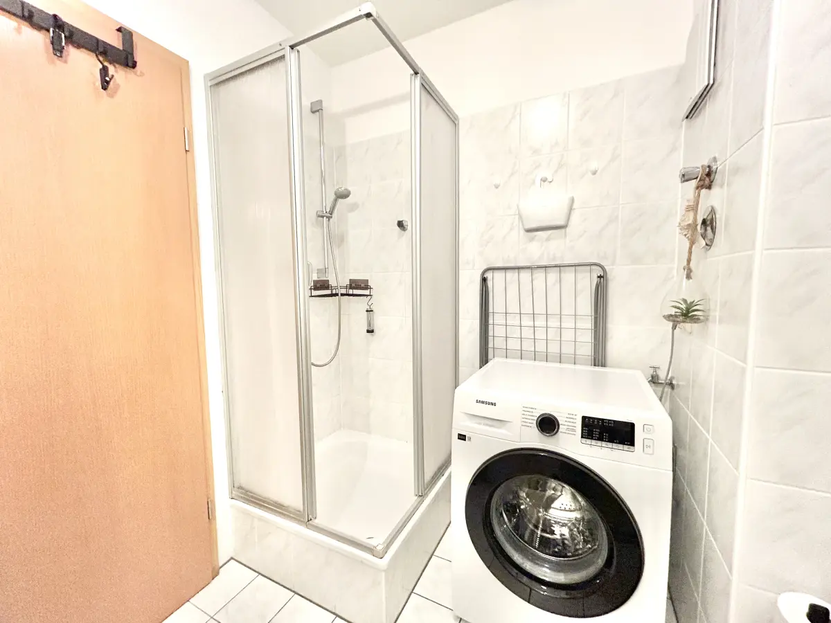 ferienwohnung-cottbus-green-apartment-bad-waschmaschine Modernes Badezimmer im Green Apartment Cottbus mit Glasdusche und eigener Waschmaschine für Langzeitgäste.