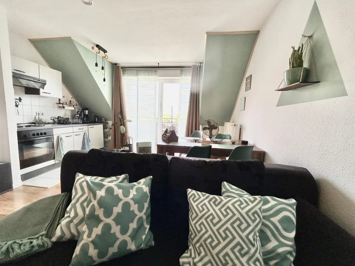 ferienwohnung-cottbus-green-apartment-profilbild Offener Wohn- und Essbereich im Green Apartment Cottbus mit voll ausgestatteter Küche, gemütlichem Sofa und Zugang zum Balkon.