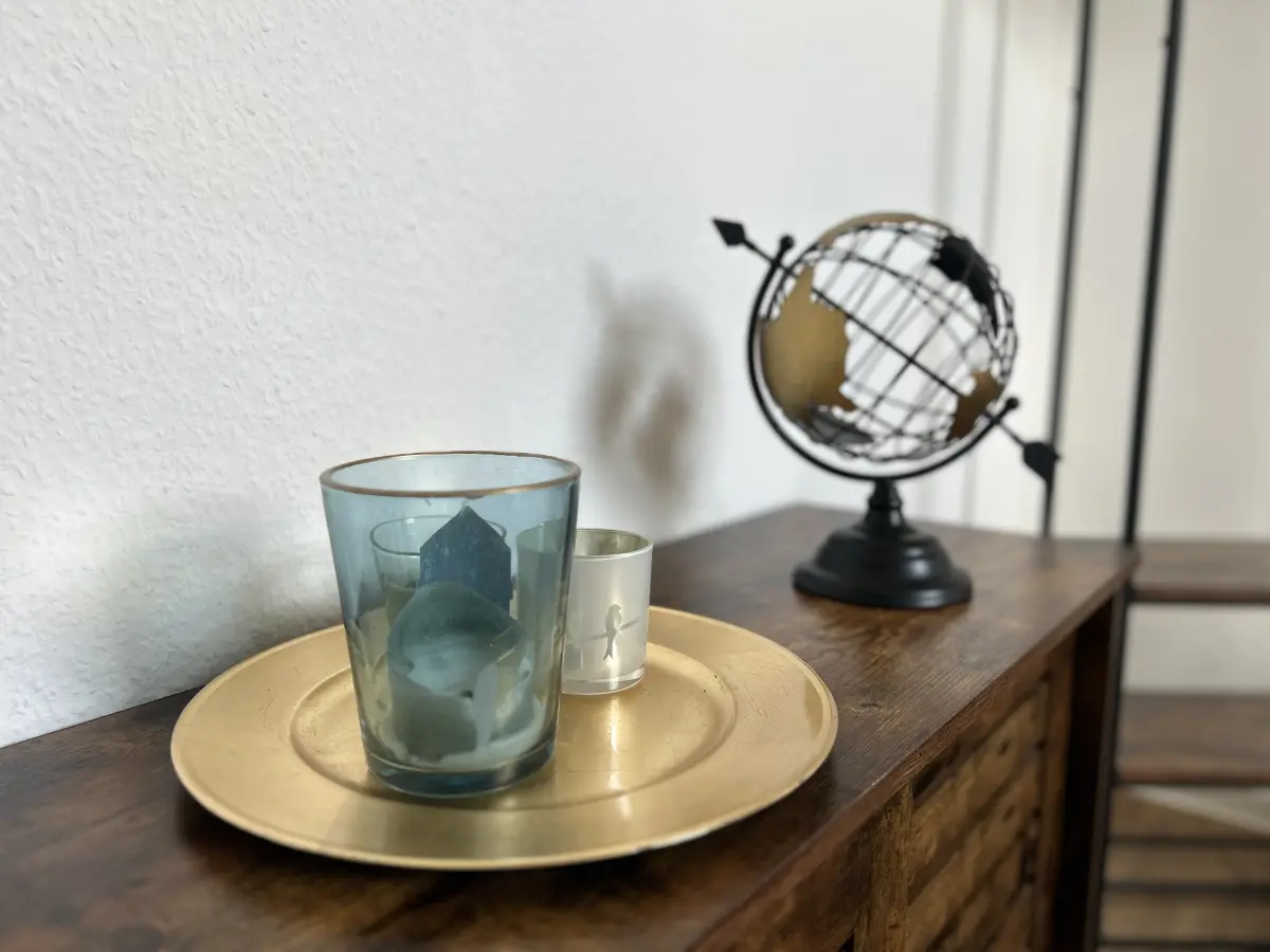 ferienwohnung-cottbus-green-apartment-schlafzimmer-deko Dekoration mit Globus und Kerze auf einer Holzkommode im Schlafzimmer des Green Apartments – Ihre stilvolle Ferienwohnung in Cottbus.