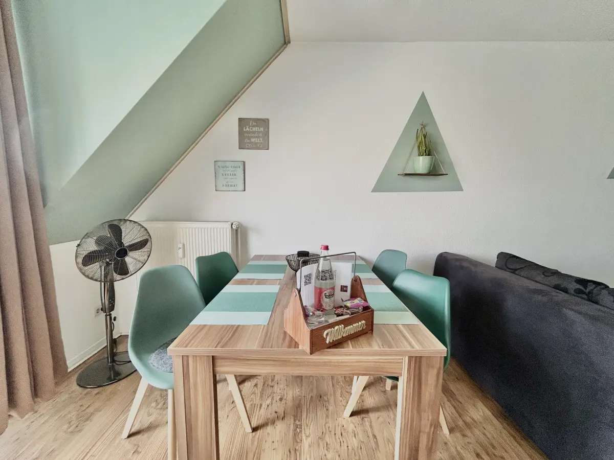 ferienwohnung-cottbus-green-apartment-wohnzimmer-esstisch-willkommen Moderner Esstisch mit grünen Stühlen im Wohnzimmer des Green Apartments, eine ruhig und zentral gelegene Ferienwohnung in Cottbus.